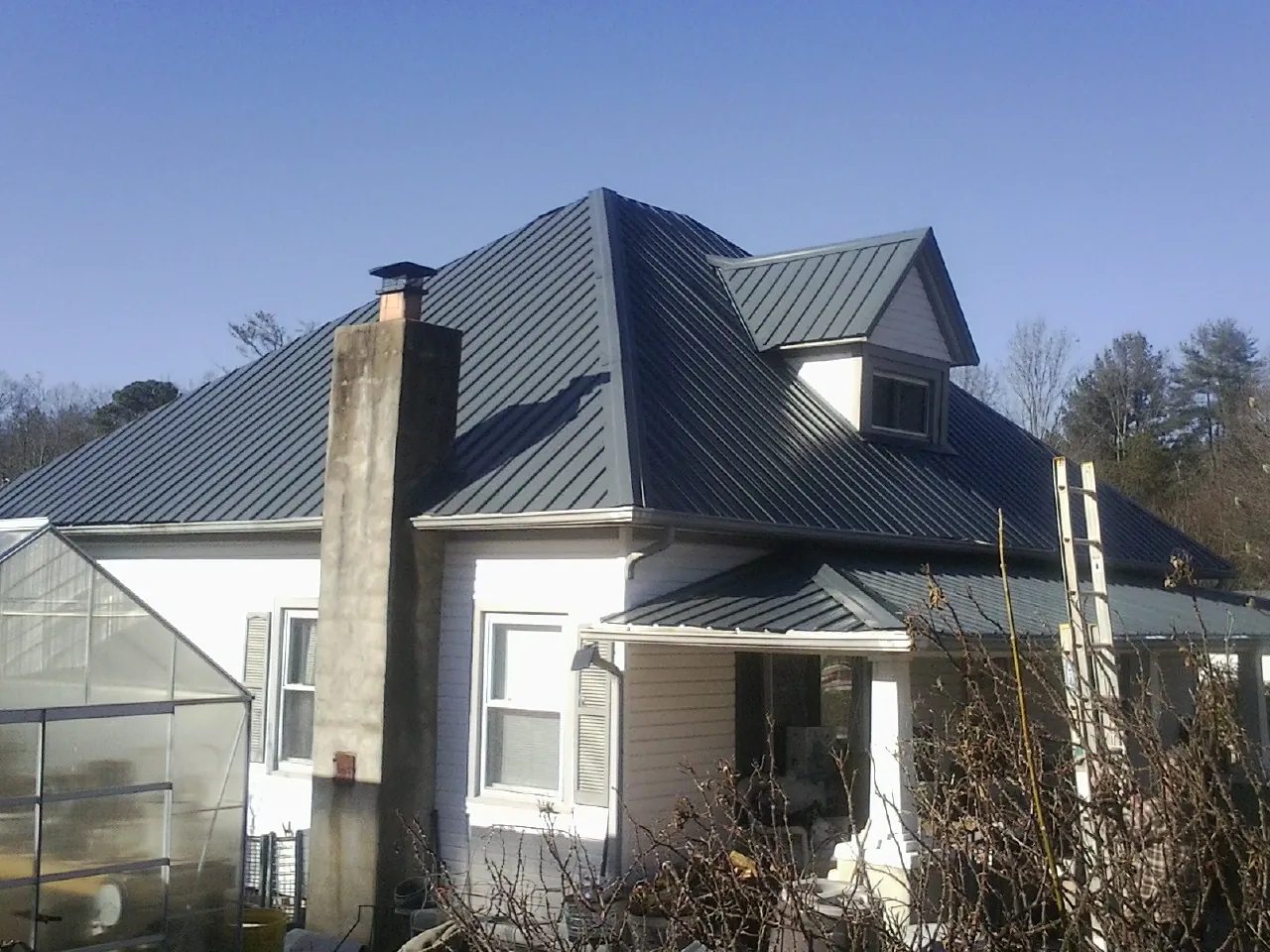 Dark blue standing seam metal roof on a white farmhouse with dormer — Slate & Tile Roof Repair by Roofing Brothers in Hollansburg