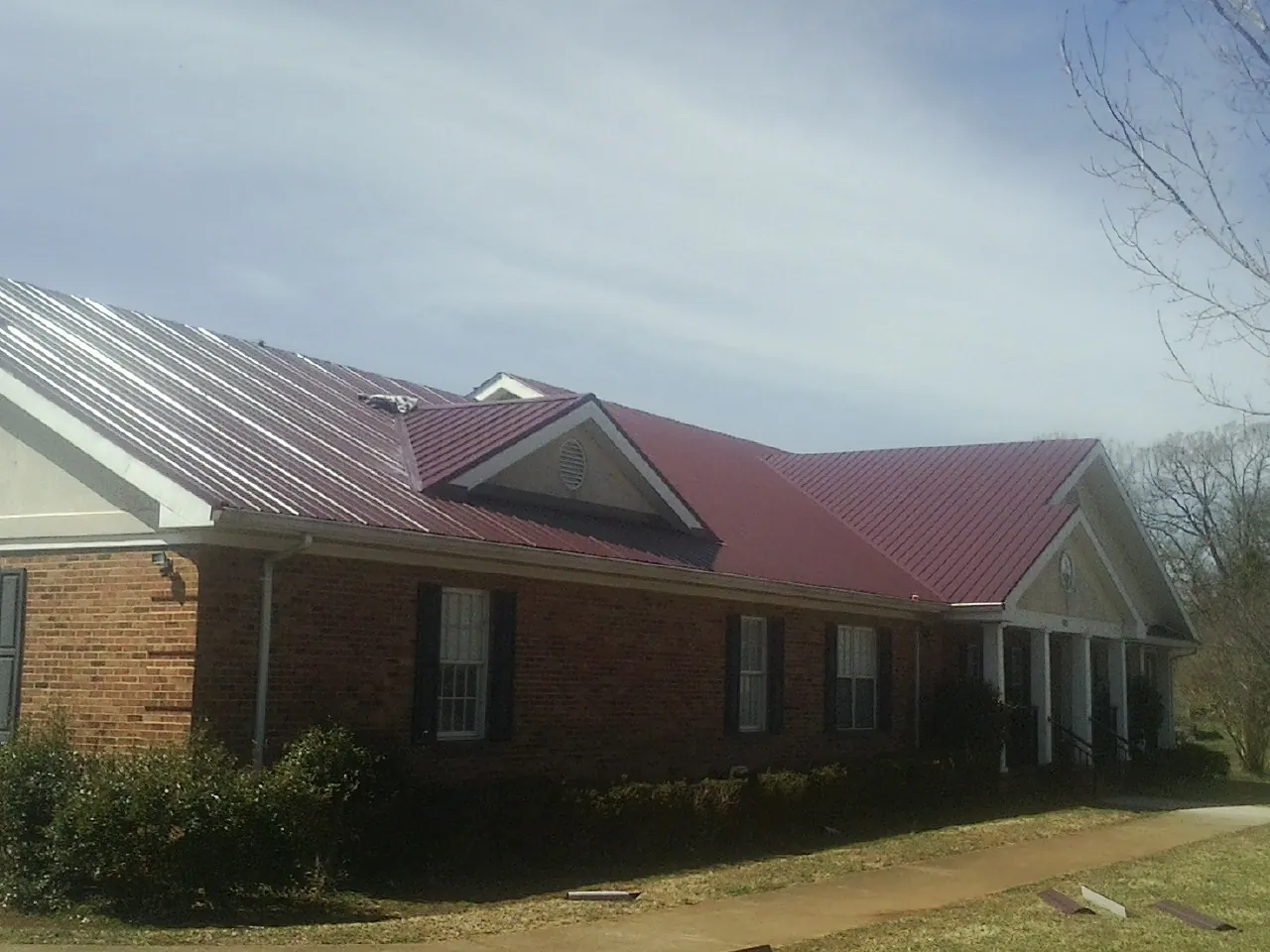 Red metal roof with gabled entries on a long brick building, from a Hail Damage Roof Repair job in Hollansburg
