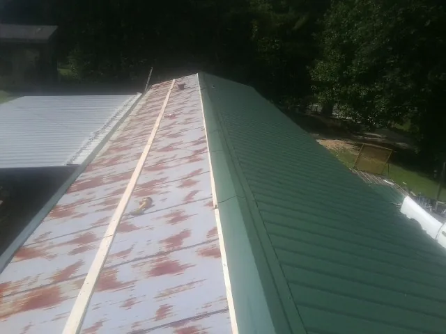 Old rusted panels beside newly installed green metal roofing — Wind Damage Roof Repair by Roofing Brothers in Hollansburg