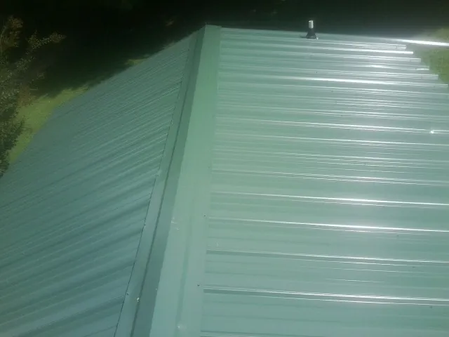 New green metal panels meeting at the ridge of a roof — Flat Roof Repair work by our crew in Hollansburg