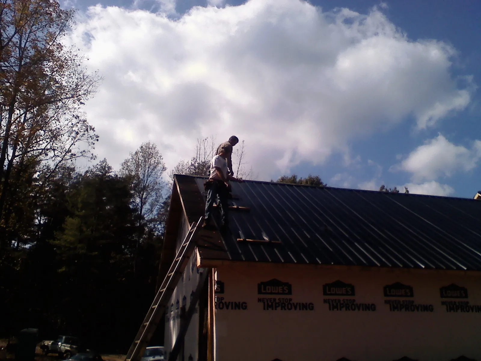 Roofer fastening dark metal panels high against a cloudy sky, from a Roof Inspection job in Hollansburg