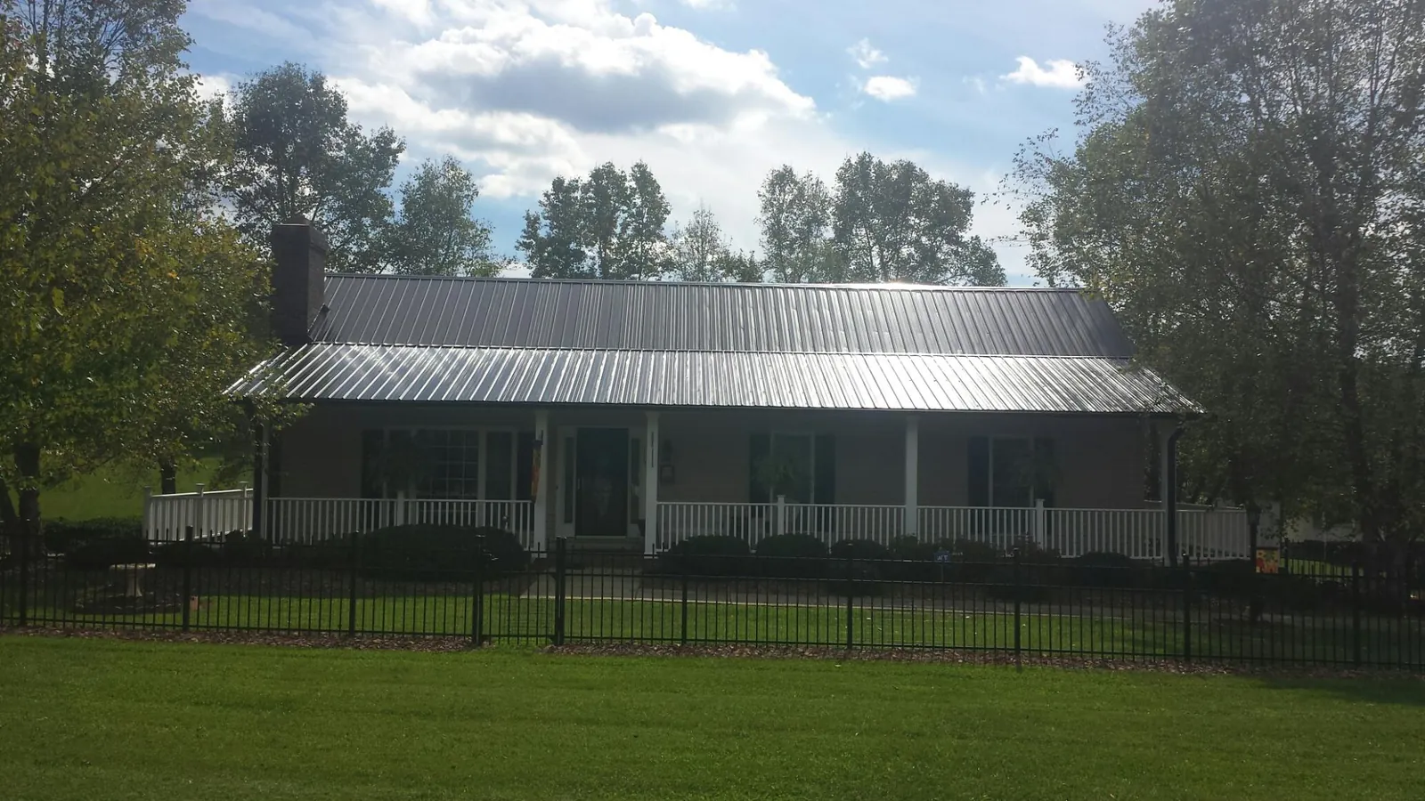 Gray metal roof on a brick ranch with a full width front porch — Gutter Guard Installation work by our crew in Hollansburg