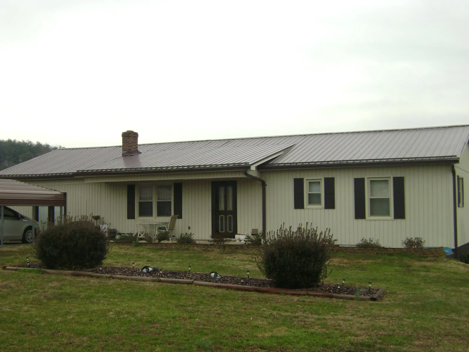 Brown metal roof on a cream sided ranch home with a brick chimney in Hollansburg