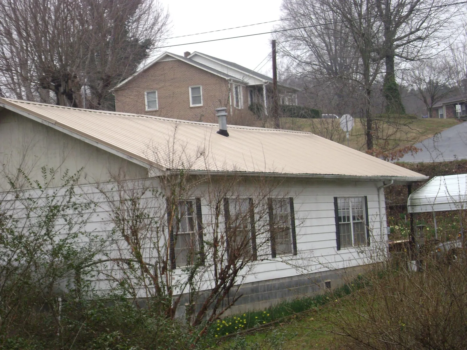 Tan metal roof on a white sided house set into a hillside — Commercial Roofing by Roofing Brothers in Hollansburg