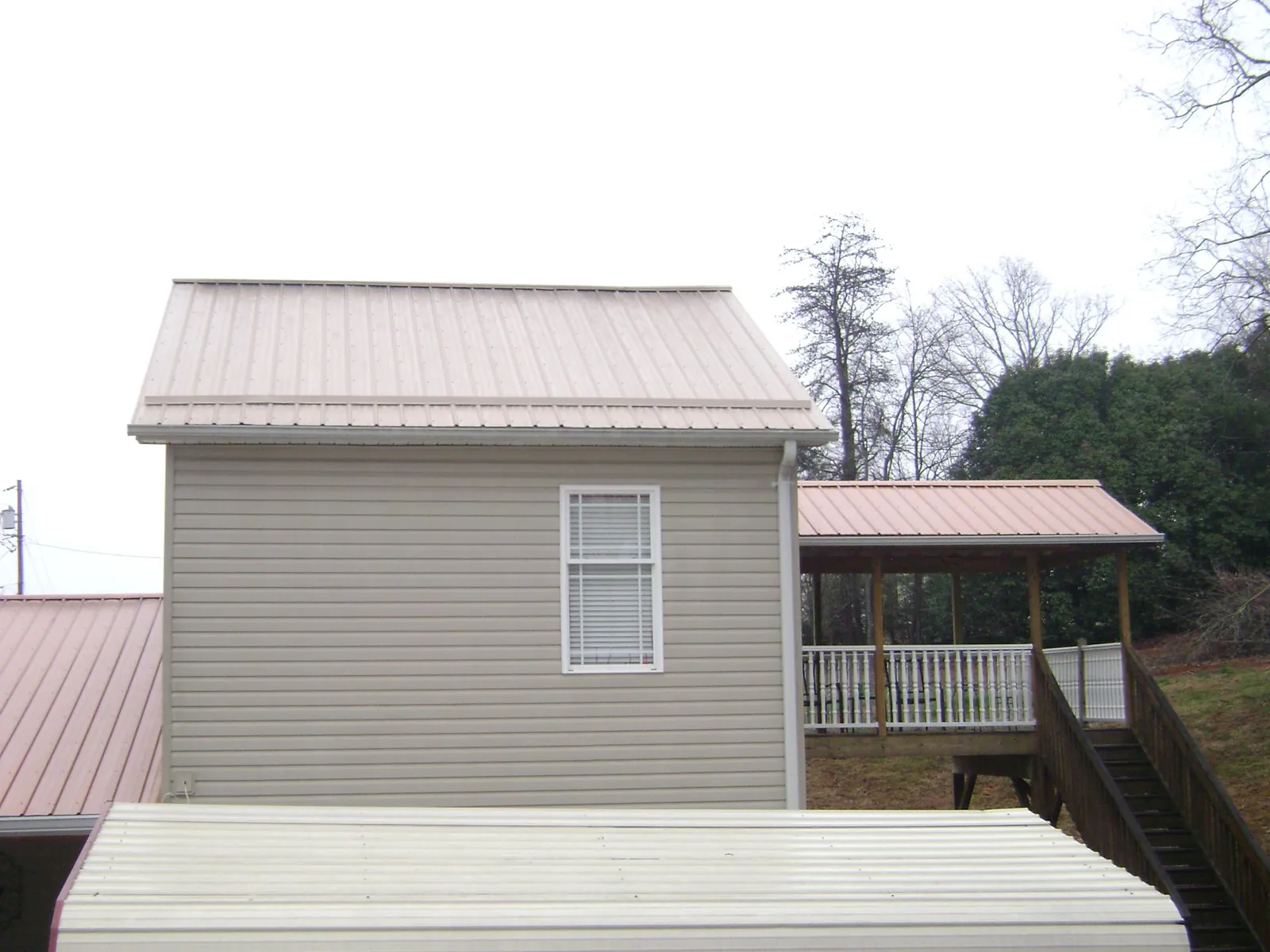 Tan metal roofs on a two story addition and attached porch, from a Roof Replacement job in Hollansburg